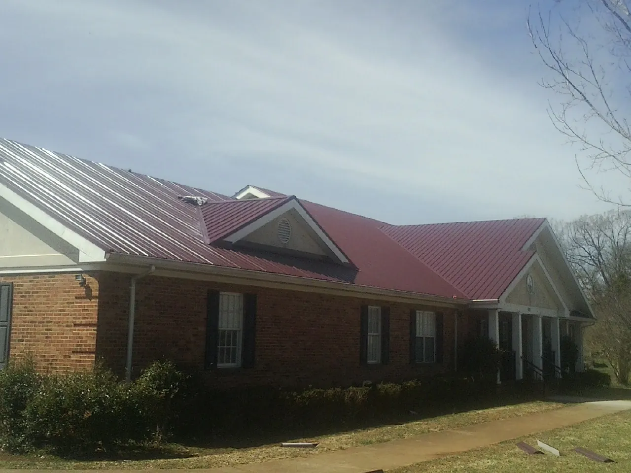 Red metal roof with gabled entries on a long brick building, from a Hail Damage Roof Repair job in Pharr