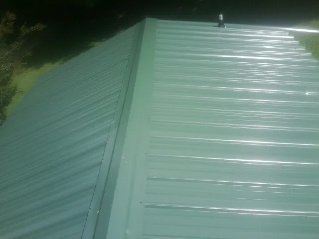 New green metal panels meeting at the ridge of a roof — Flat Roof Repair work by our crew in Pharr